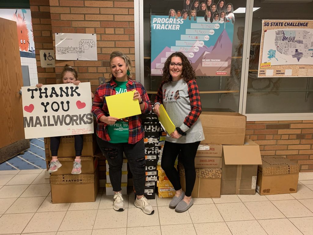 three people posing with boxes of paper with a thank you mailworks sign.