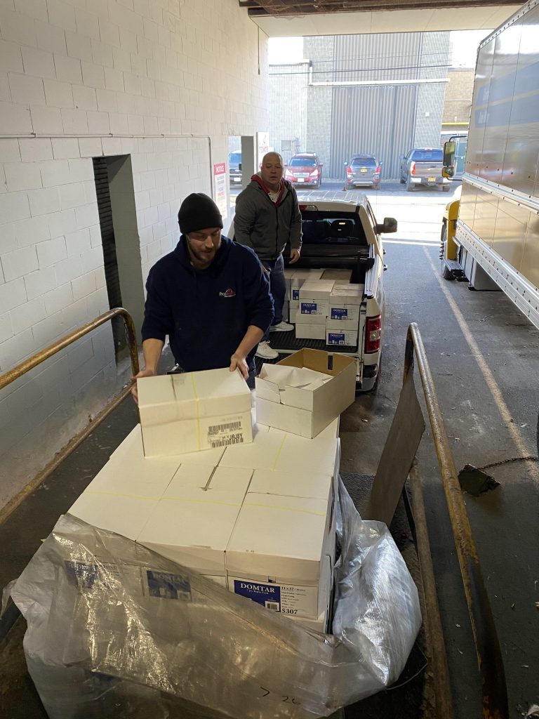 a palette of paper being loaded into a truck by 2 men.