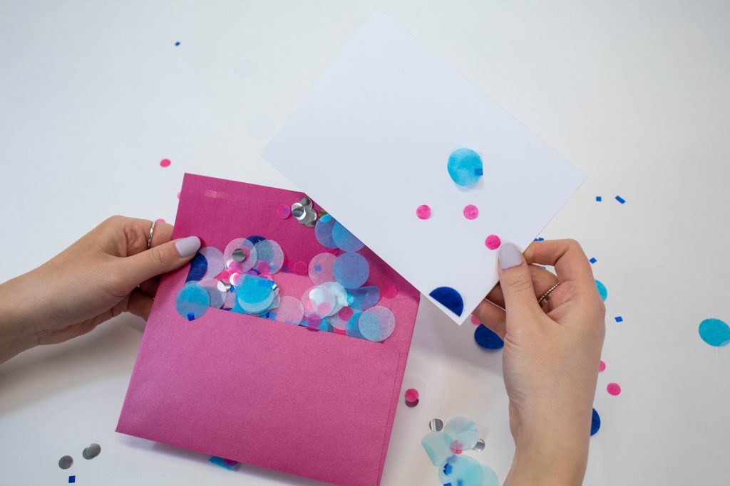 Hannah holding a pink envelope and a white card. Confetti is pouring out of the envelope. 